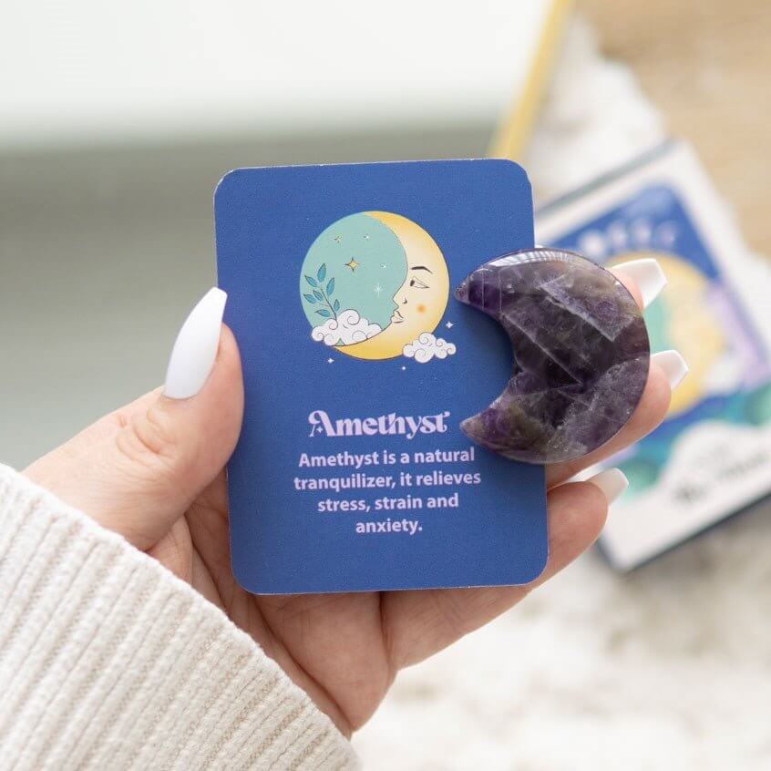 Hand holding an amethyst crystal with a card explaining its properties.