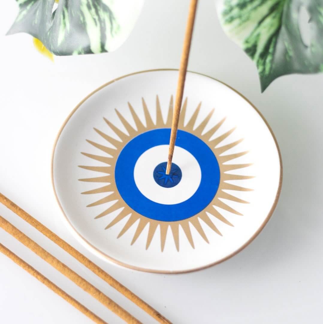 Decorative plate with sunburst design and blue center, featuring an incense stick.