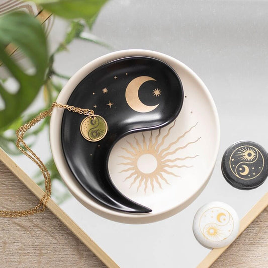 Yin yang dish with celestial design, gold necklace, and decorative stones on a light background